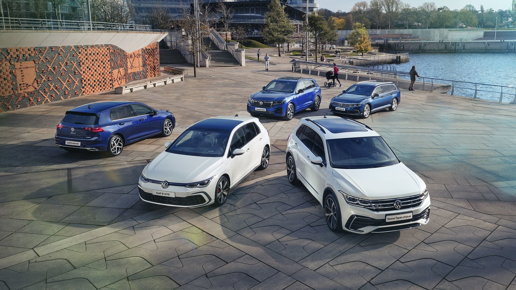 Cinque modelli Volkswagen fermi in un parcheggio. Sullo sfondo uno spazio cittadino.