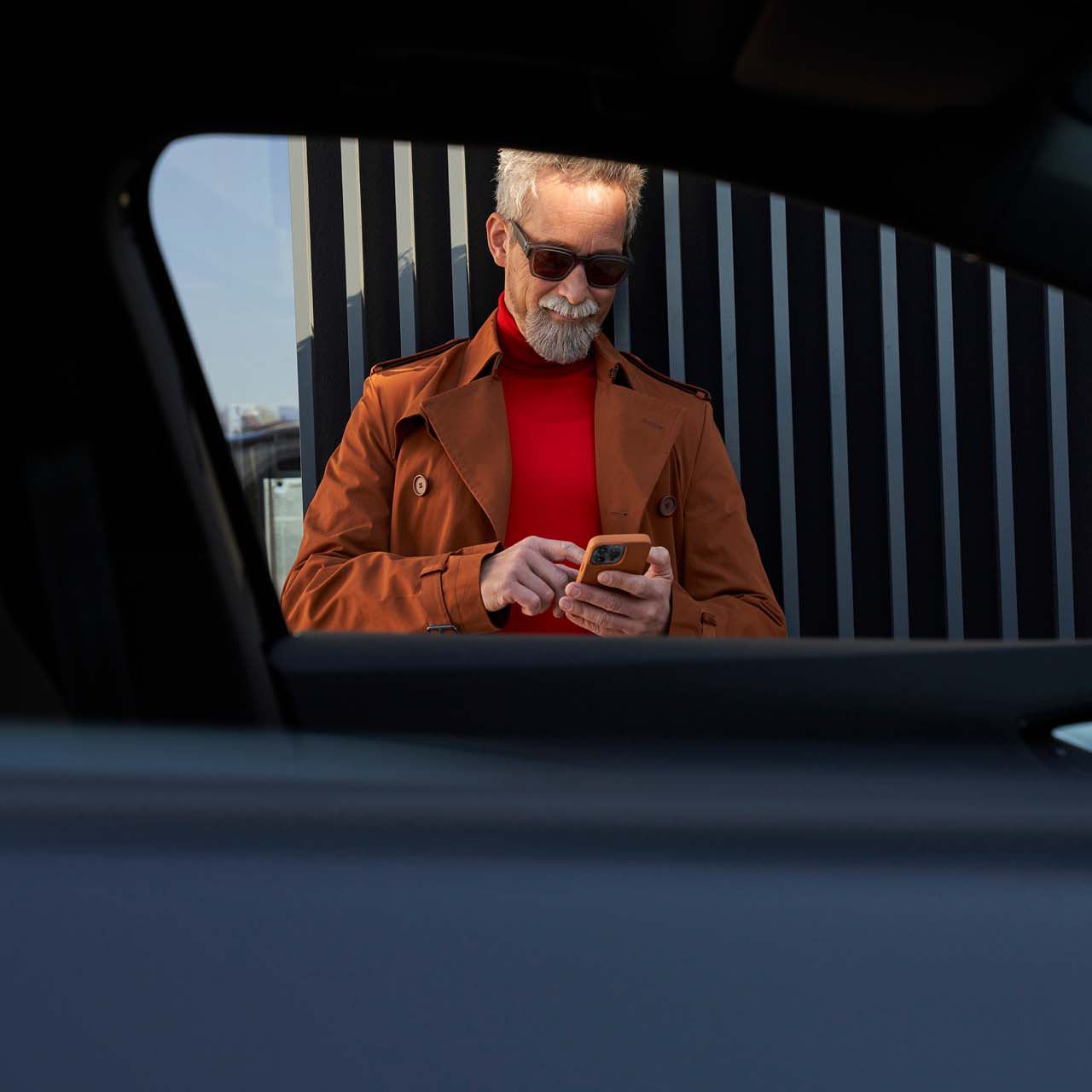 Un uomo consulta il suo smartphone accanto alla sua VW