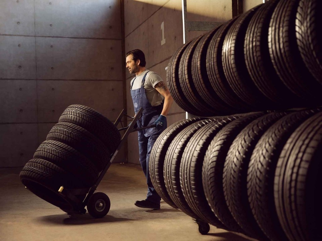 Un operaio di Volkswagen Service trasporta una pila di pneumatici su un carrellino.