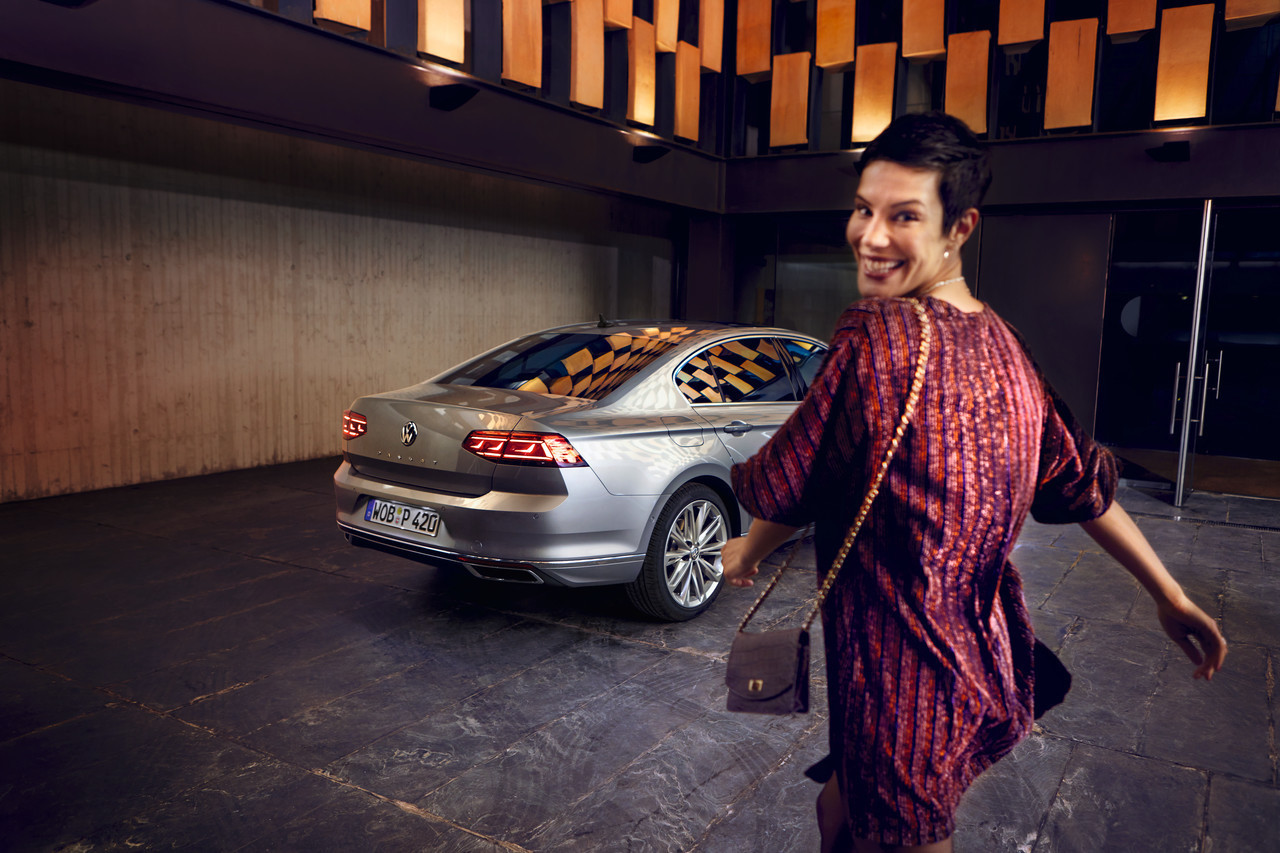Una donna si avvicina sorridendo ad una VW Nuova Passat parcheggiata in città